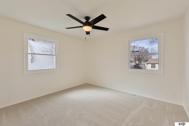 carpeted spare room featuring visible vents, plenty of natural light, baseboards, and a ceiling fan