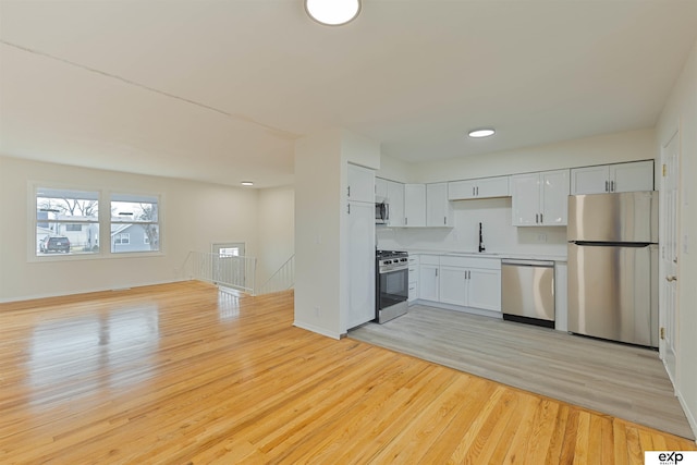 kitchen with light countertops, light wood-style flooring, white cabinets, stainless steel appliances, and a sink