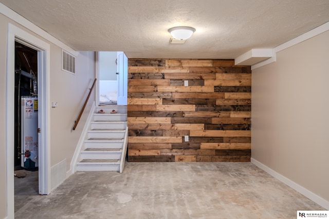 below grade area with wooden walls, visible vents, stairs, water heater, and a textured ceiling