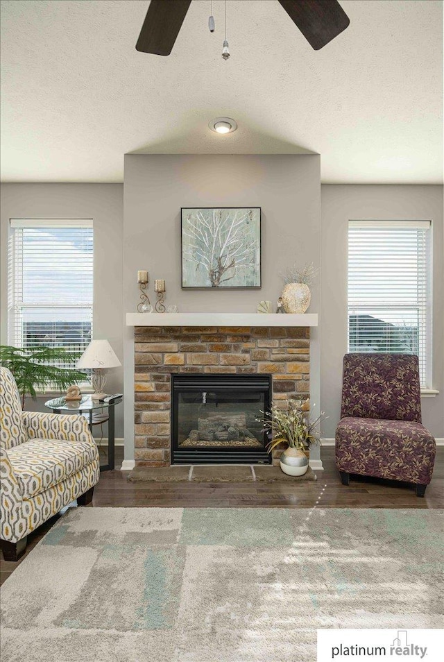 living area featuring wood finished floors, ceiling fan, a fireplace, and baseboards