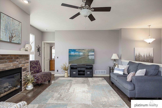 living room featuring baseboards, a stone fireplace, a ceiling fan, visible vents, and wood finished floors