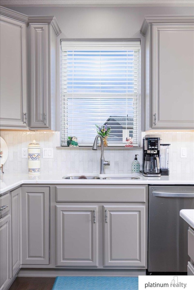 kitchen with stainless steel dishwasher, gray cabinets, light countertops, a sink, and backsplash