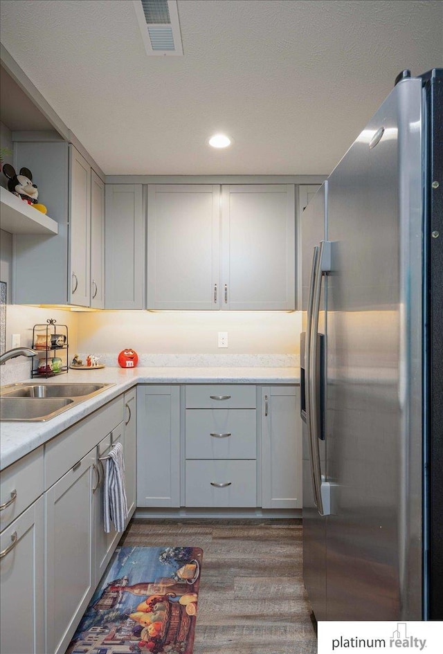 kitchen with visible vents, stainless steel fridge, a sink, dark wood-style flooring, and light countertops