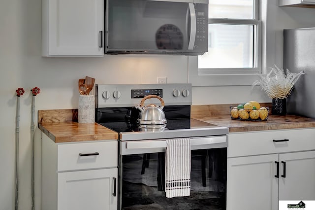 kitchen featuring wooden counters, stainless steel range with electric stovetop, and white cabinetry