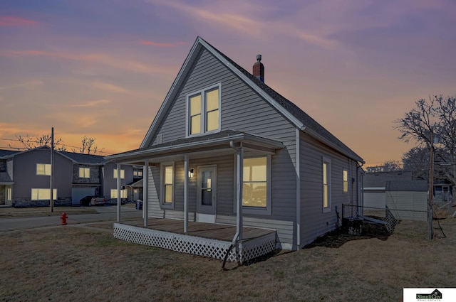 view of front facade featuring covered porch, a chimney, and a front lawn