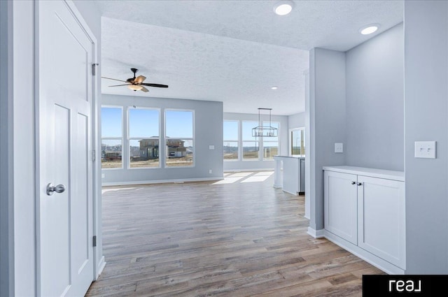 hall featuring recessed lighting, baseboards, light wood-style floors, and a textured ceiling