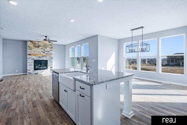 kitchen featuring wood finished floors, light stone countertops, a sink, dishwasher, and ceiling fan with notable chandelier