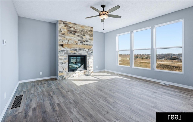 unfurnished living room with visible vents, baseboards, ceiling fan, a fireplace, and wood finished floors