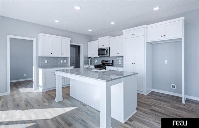 kitchen featuring light stone counters, appliances with stainless steel finishes, white cabinets, and an island with sink