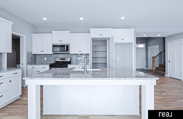 kitchen with light wood finished floors, white cabinets, stainless steel appliances, and an island with sink