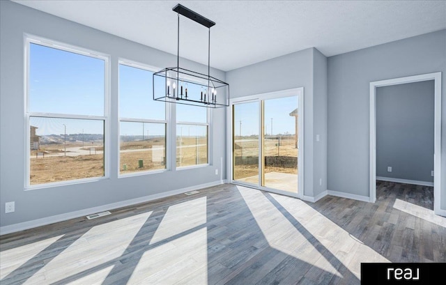 unfurnished dining area featuring visible vents, baseboards, an inviting chandelier, and wood finished floors