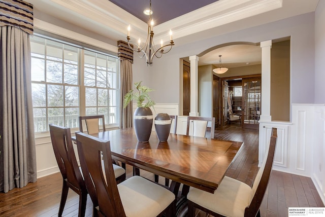 dining space with a tray ceiling, decorative columns, arched walkways, and dark wood-type flooring