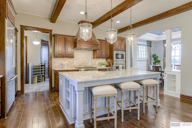 kitchen with tasteful backsplash, beamed ceiling, an island with sink, stainless steel appliances, and dark wood-style flooring