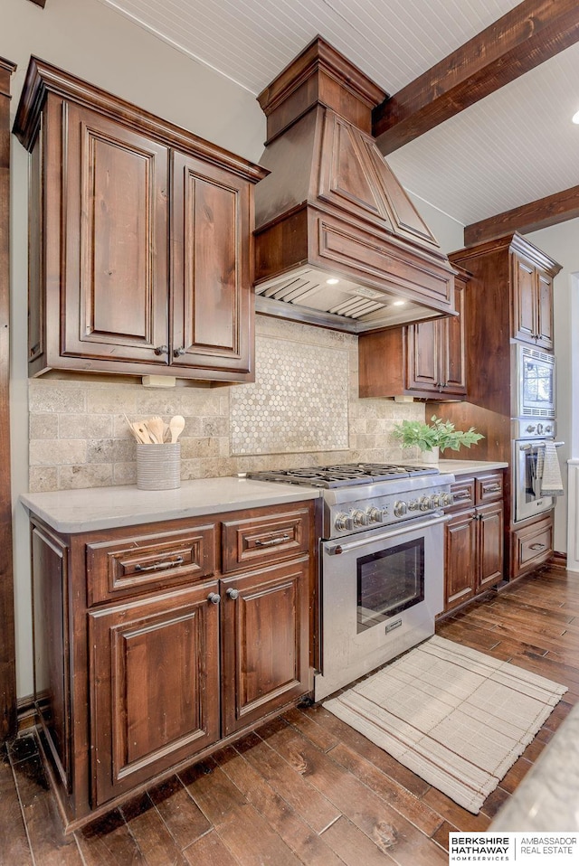 kitchen with dark wood-style floors, decorative backsplash, light countertops, custom range hood, and appliances with stainless steel finishes