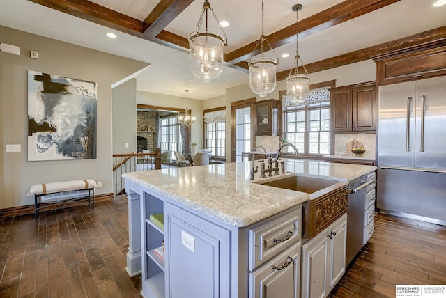 kitchen featuring dark wood finished floors, a kitchen island with sink, a sink, built in refrigerator, and tasteful backsplash