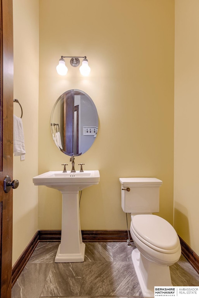 half bathroom with a sink, baseboards, and toilet