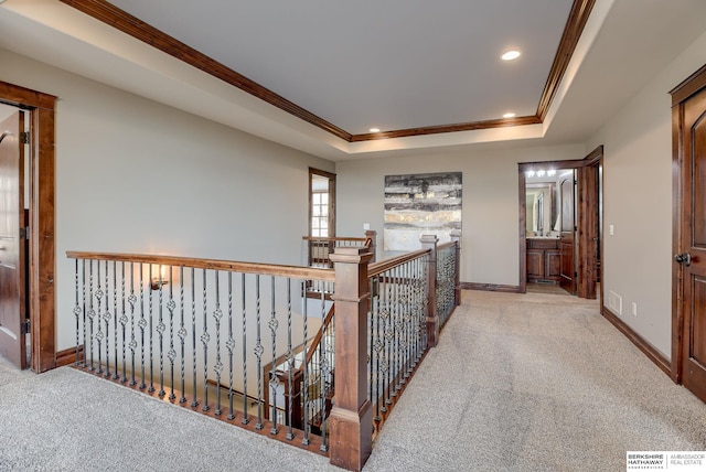 hall featuring a tray ceiling, crown molding, carpet flooring, and an upstairs landing