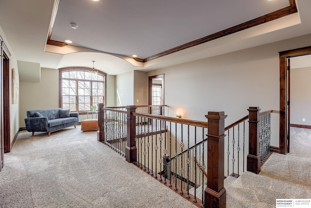 corridor with crown molding, baseboards, an upstairs landing, carpet flooring, and a raised ceiling