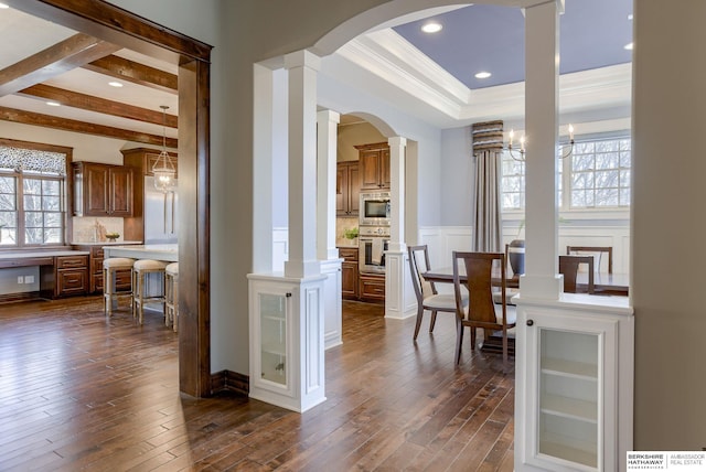 dining room featuring decorative columns, dark wood-type flooring, a wainscoted wall, and a decorative wall