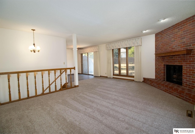 unfurnished living room featuring a brick fireplace, carpet flooring, visible vents, and a chandelier