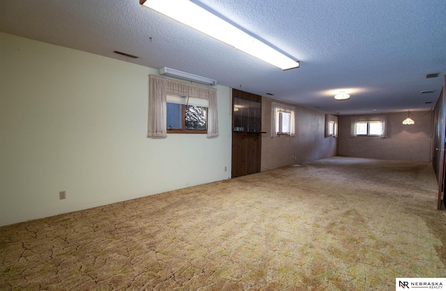 below grade area featuring carpet flooring, a textured ceiling, and visible vents