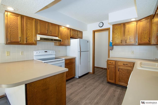 kitchen with white appliances, a peninsula, a sink, light countertops, and under cabinet range hood