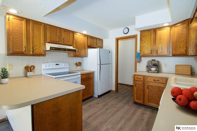 kitchen featuring white appliances, light countertops, under cabinet range hood, and a sink