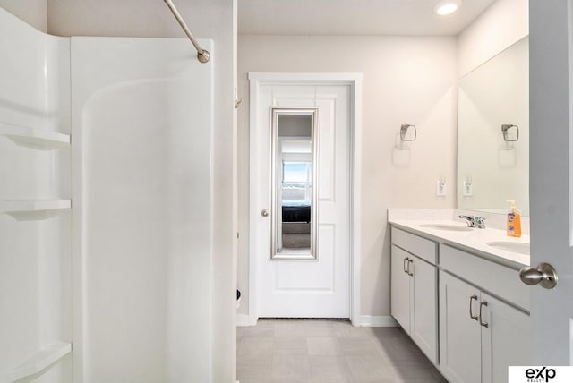 bathroom featuring baseboards, double vanity, tile patterned floors, walk in shower, and a sink