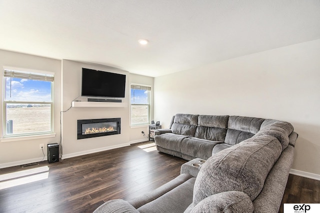 living room featuring visible vents, baseboards, recessed lighting, dark wood-type flooring, and a glass covered fireplace