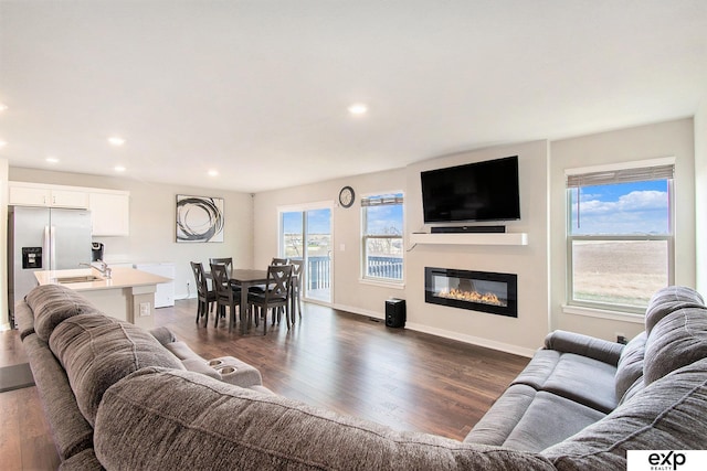 living room featuring baseboards, dark wood-style floors, a glass covered fireplace, and recessed lighting