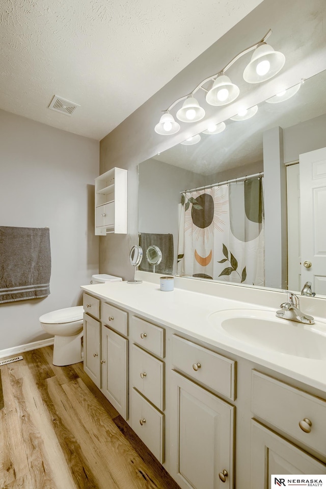 bathroom with visible vents, toilet, vanity, wood finished floors, and a textured ceiling