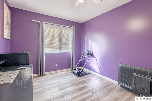 exercise room featuring ceiling fan, a textured ceiling, baseboards, and light wood-style floors