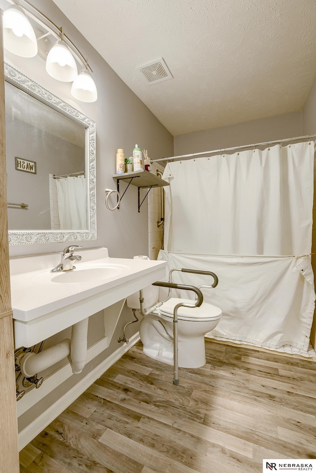 bathroom with visible vents, baseboards, toilet, wood finished floors, and a textured ceiling