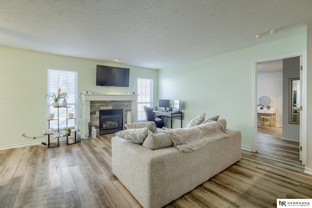 living area featuring a glass covered fireplace, a textured ceiling, a healthy amount of sunlight, and wood finished floors