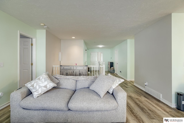 living area with visible vents, a textured ceiling, light wood-type flooring, and baseboards