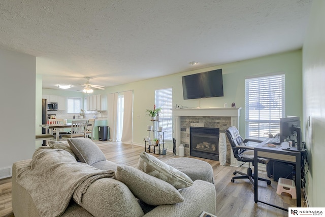 living room with light wood-type flooring, plenty of natural light, and a stone fireplace