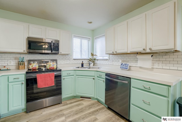 kitchen featuring light wood-type flooring, light countertops, stainless steel appliances, white cabinetry, and a sink