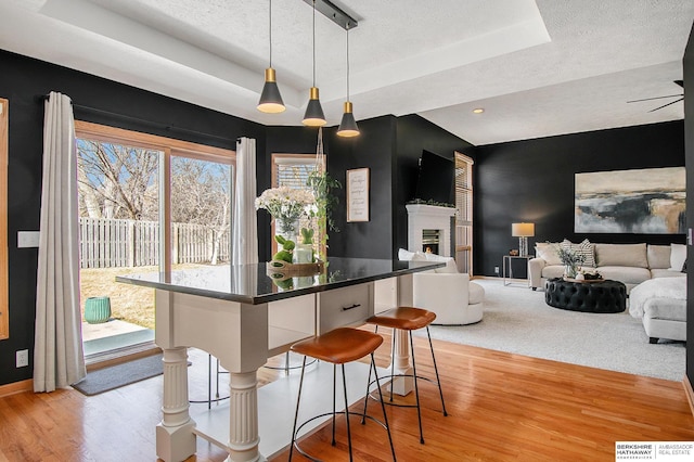 kitchen featuring a kitchen bar, a tray ceiling, light wood finished floors, and a warm lit fireplace