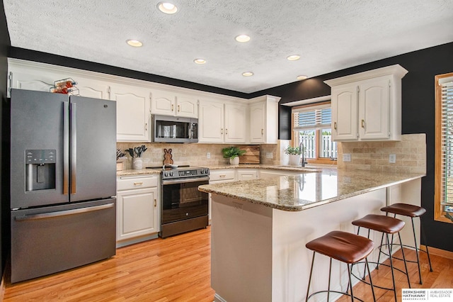 kitchen featuring white cabinets, a peninsula, stainless steel appliances, and a sink