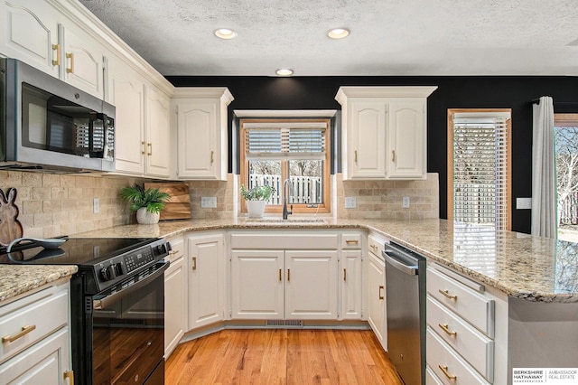 kitchen with light wood-type flooring, a peninsula, white cabinets, stainless steel appliances, and a sink