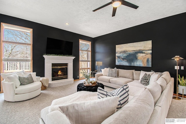 carpeted living room with a wealth of natural light, a brick fireplace, a textured ceiling, and a ceiling fan