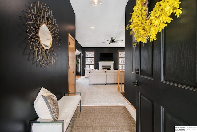 carpeted entrance foyer with a lit fireplace and a ceiling fan