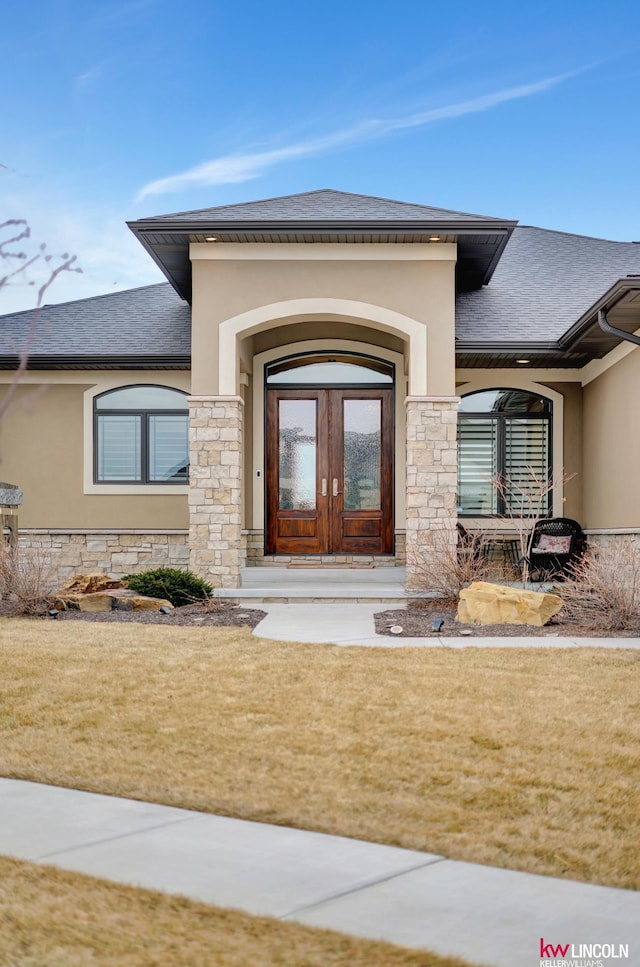 property entrance with stucco siding, stone siding, and roof with shingles