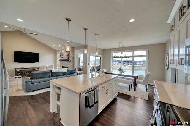 kitchen with a sink, a stone fireplace, stainless steel dishwasher, white cabinetry, and dark wood-style flooring