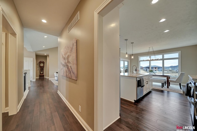 hallway featuring dark wood finished floors, visible vents, baseboards, and a sink