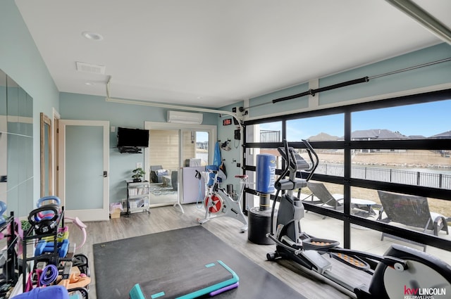 exercise area with a wall mounted air conditioner, visible vents, and wood finished floors