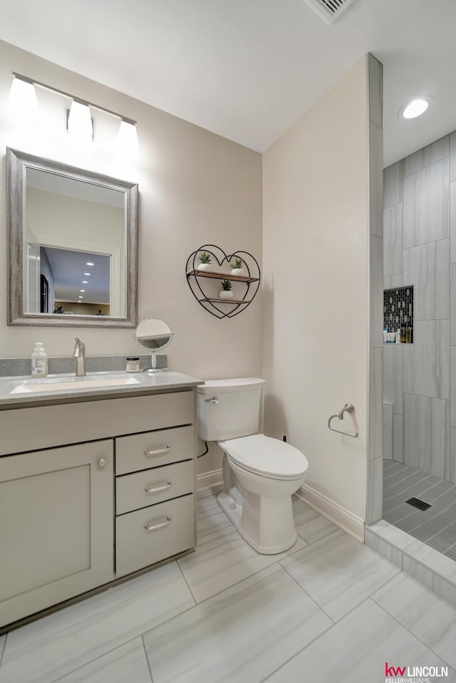 bathroom featuring a tile shower, toilet, vanity, and baseboards