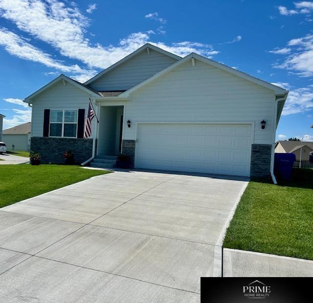 view of front of house featuring stone siding, a garage, driveway, and a front yard