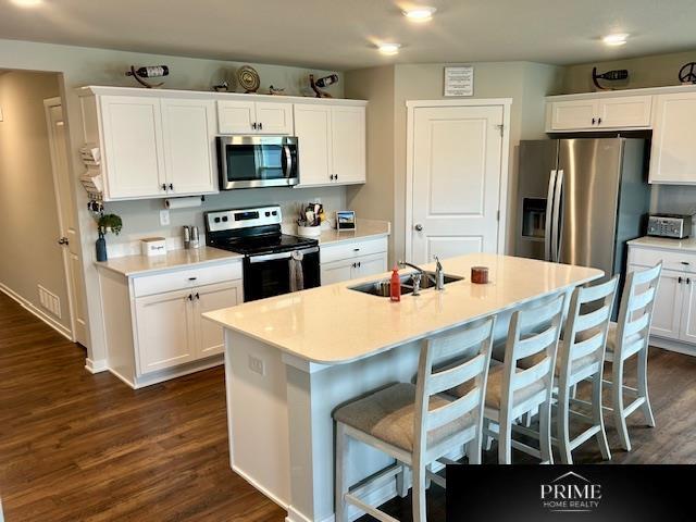 kitchen featuring a sink, stainless steel appliances, dark wood-type flooring, white cabinetry, and a kitchen breakfast bar