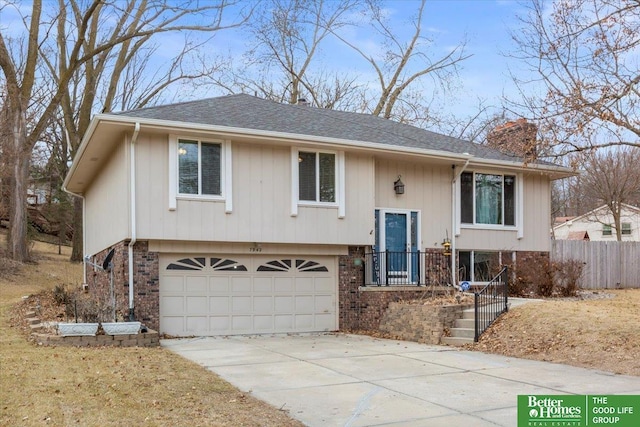 split foyer home with fence, concrete driveway, an attached garage, brick siding, and a chimney